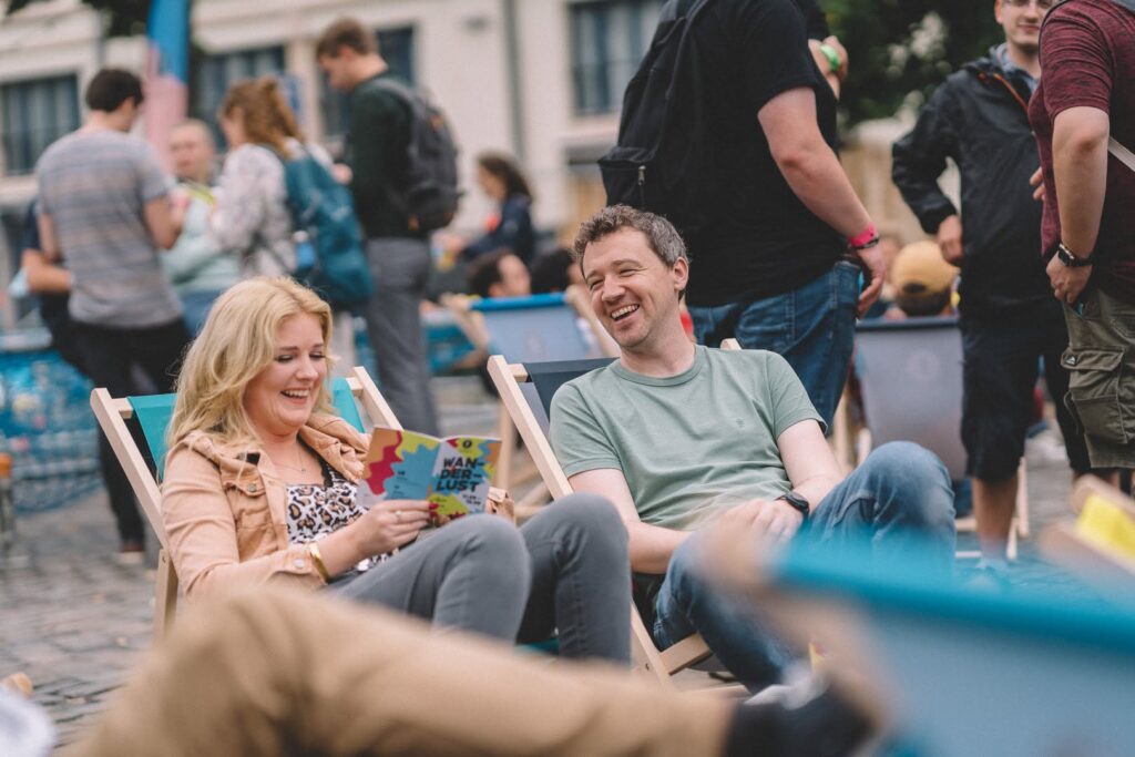 Festivalgoers in deckchairs reading the Wanderlust programme